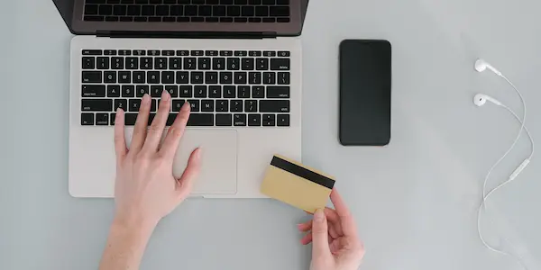 Τα χέρια ενός ατόμου με μια τραπεζική κάρτα και έναν φορητό υπολογιστή.