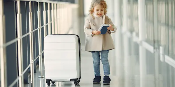 Χαρούμενο κοριτσάκι με βαλίτσα και διαβατήριο στο αεροδρόμιο.